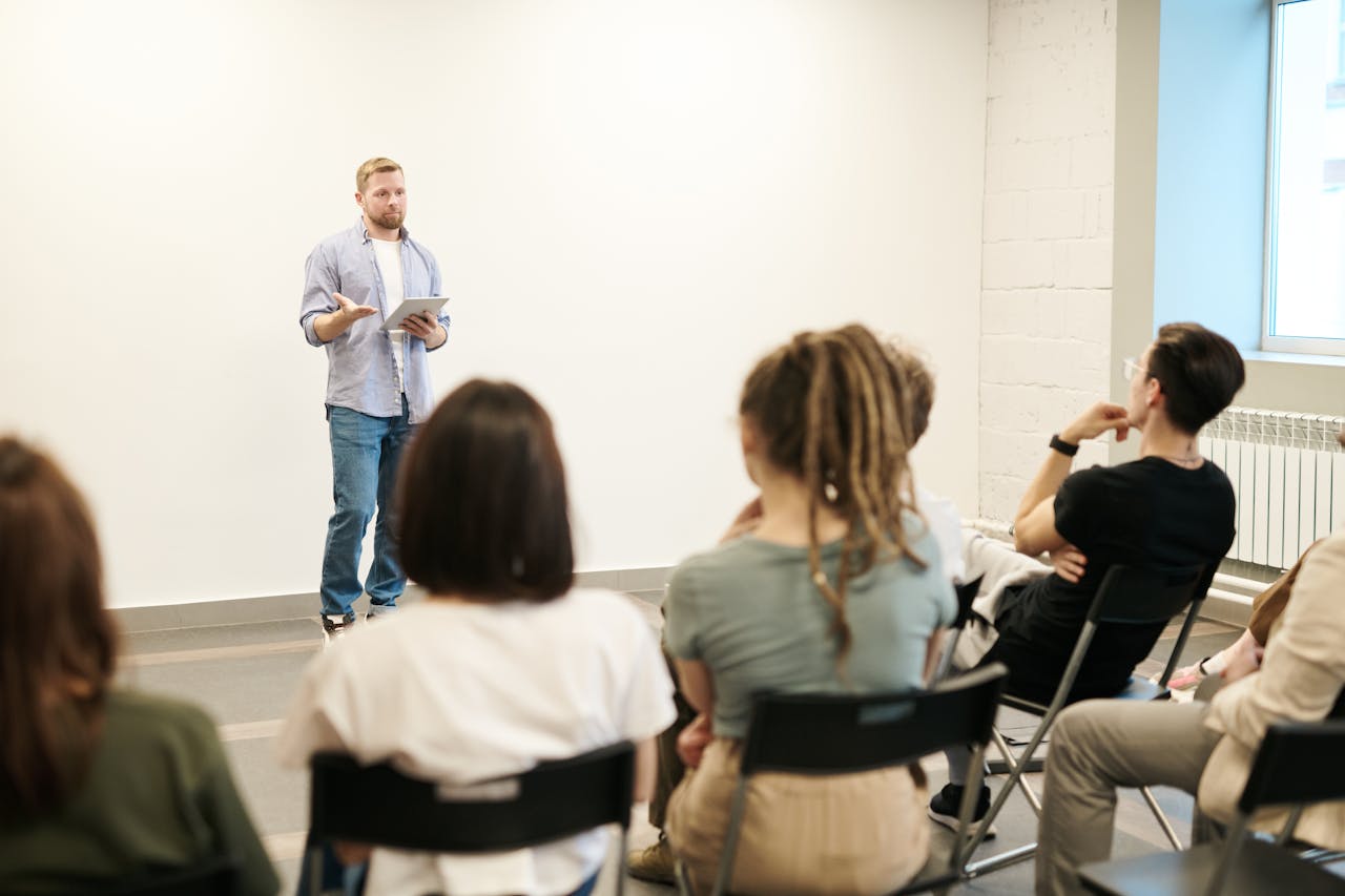 Mastering the First Impression: Your intriguing post title goes here Man presenting with tablet to a small seated audience in a modern indoor setting.